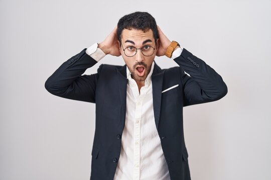 Handsome business hispanic man standing over white background crazy and scared with hands on head, afraid and surprised of shock with open mouth