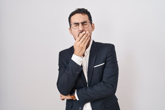 Handsome business hispanic man standing over white background bored yawning tired covering mouth with hand. restless and sleepiness.