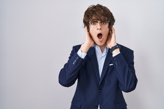 Hispanic business young man wearing glasses crazy and scared with hands on head, afraid and surprised of shock with open mouth