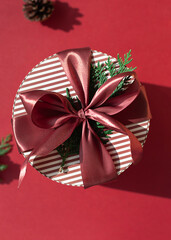 Christmas round gift box with bow on the red background. Close up winter holidays greeting card.