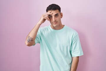 Handsome hispanic man standing over pink background worried and stressed about a problem with hand on forehead, nervous and anxious for crisis