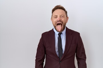 Middle age business man with beard wearing suit and tie sticking tongue out happy with funny expression. emotion concept.