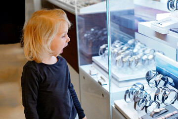 A surprised little girl looks at an expensive watch in a store window.