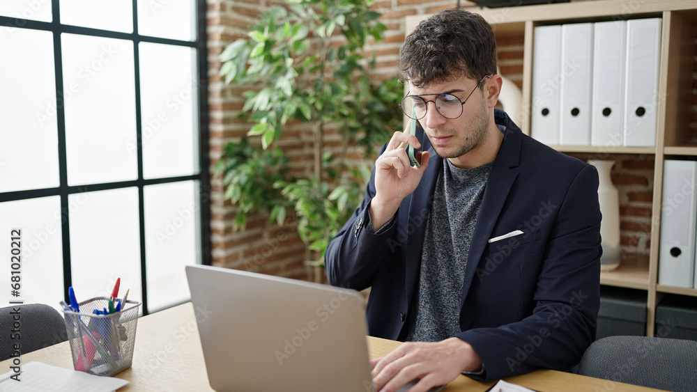 Wall mural Young hispanic man business worker talking on the phone using laptop at office