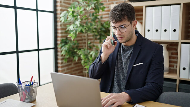 Young hispanic man business worker talking on the phone using laptop at office