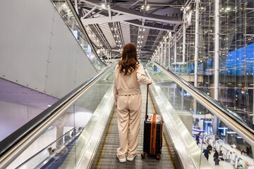Women drag suitcases up escalators at the airport in preparation to board flights for sightseeing and business trips. - obrazy, fototapety, plakaty
