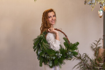 Portrait of young woman holding asymmetrical green Christmas wreath made of natural materials on...