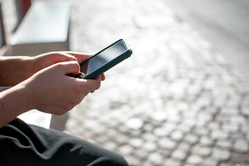 Close up view of hands using cell phone with body seated background on street