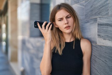 Fototapeta premium Young blonde woman listening to voice message with serious face at street