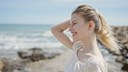 Fototapeta na wymiar Young blonde woman tourist smiling confident touching hair at beach
