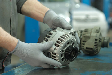 An auto mechanic replaces a faulty generator during car repair at a service center. Inspection and...
