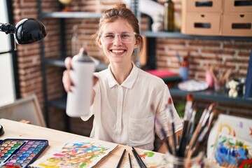 Young blonde woman artist smiling confident holding graffiti spray at art studio