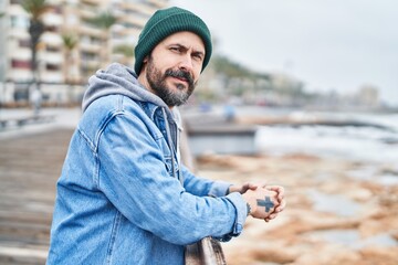 Young bald man leaning on balustrade with serious expression at seaside