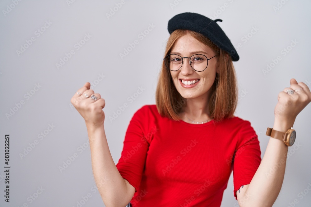 Poster young redhead woman standing wearing glasses and beret celebrating surprised and amazed for success 