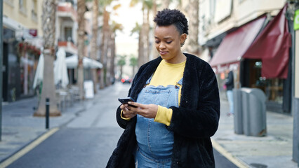 Young pregnant woman using smartphone smiling at street