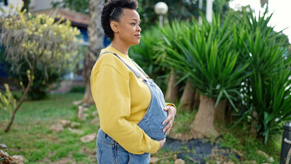 Young pregnant woman touching belly with relaxed expression at park