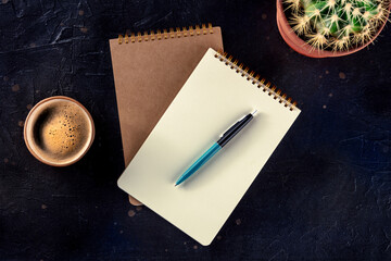 Notebook with a pen, coffee, and plant, overhead flat lay shot on a black background, a mockup