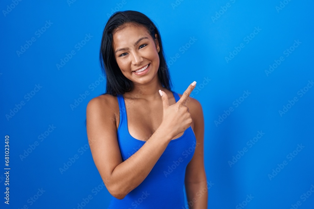 Wall mural hispanic woman standing over blue background cheerful with a smile on face pointing with hand and fi