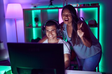 Young hispanic couple playing video games smiling with an idea or question pointing finger with happy face, number one