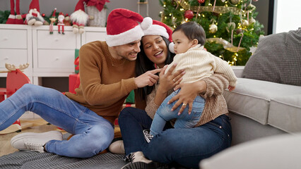 Couple and son hugging each other sitting on floor by christmas tree at home