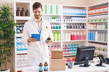 Young caucasian man pharmacist using touchpad holding medication bottle at pharmacy