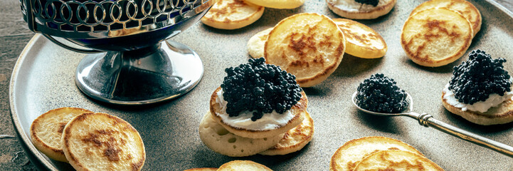 Blinis with black caviar panorama. Mini pancakes on a festive dish, an elegant appetizer