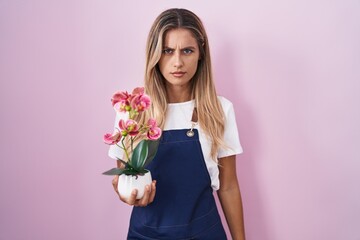 Young blonde woman wearing gardener apron holding plant skeptic and nervous, frowning upset because of problem. negative person.