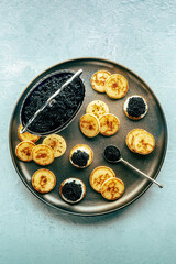 Blinis with black caviar and cream cheese, shot from the top on a festive dish, mini pancakes, an elegant appetizer