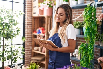 Young blonde woman florist smiling confident writing on notebook at florist