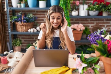 Young blonde woman working at florist shop doing video call screaming proud, celebrating victory and success very excited with raised arm