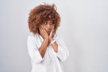 Young hispanic woman with curly hair standing over white background tired hands covering face, depression and sadness, upset and irritated for problem