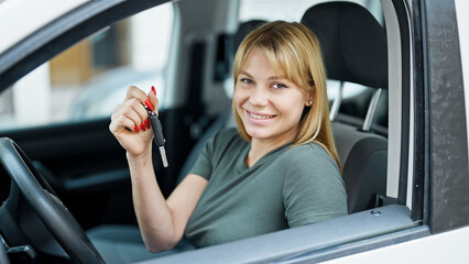 Young blonde woman smiling confident holding key of new car at street