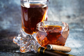 A glass of Scotch whiskey with ice and a cigar on a dark background.
