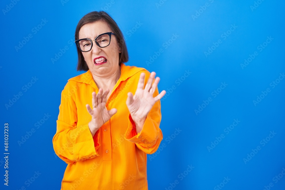 Sticker middle age hispanic woman wearing glasses standing over blue background disgusted expression, disple