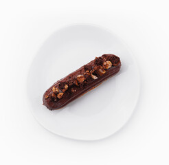 eclair with chocolate and nuts on a white plate