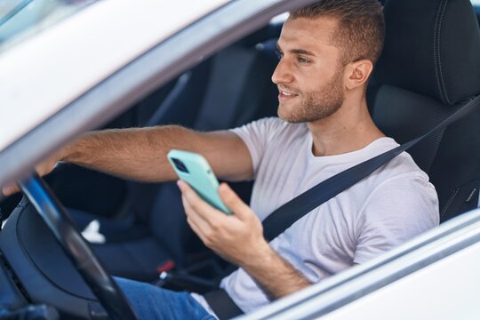 Young caucasian man using smartphone sitting on car at street
