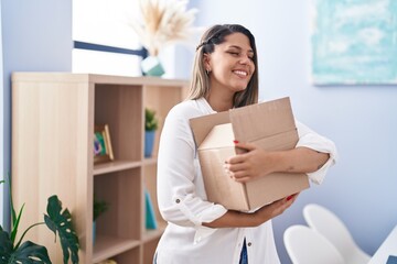 Young hispanic woman smiling confident hugging cardboard box at home