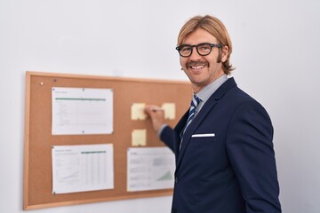 Young blond man business worker writing on cork board at office