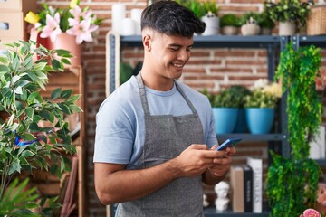 Young hispanic man florist smiling confident using smartphone at flower shop