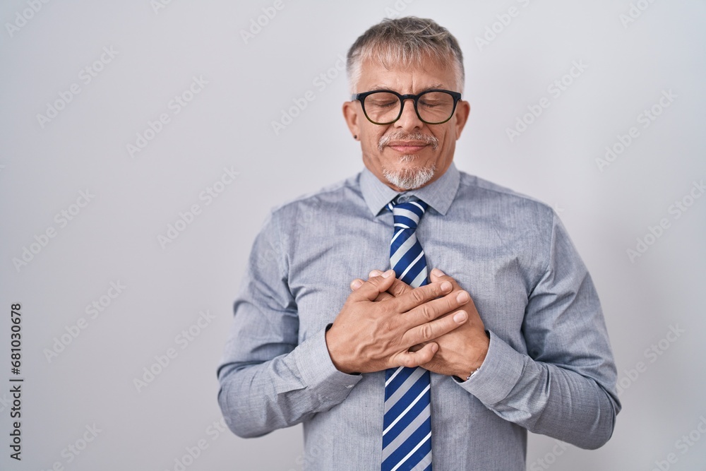 Wall mural Hispanic business man with grey hair wearing glasses smiling with hands on chest with closed eyes and grateful gesture on face. health concept.