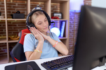 Young caucasian woman playing video games wearing headphones sleeping tired dreaming and posing with hands together while smiling with closed eyes.