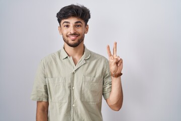 Arab man with beard standing over white background showing and pointing up with fingers number two while smiling confident and happy.