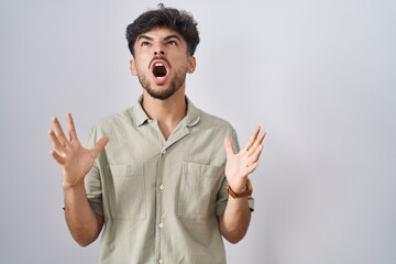Arab man with beard standing over white background crazy and mad shouting and yelling with...