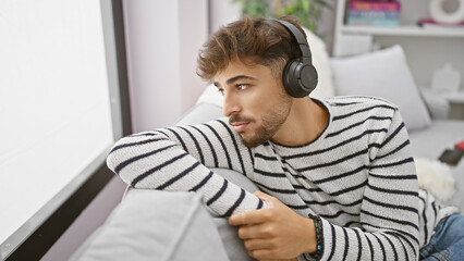 Young arab man enjoys his own sound sanctuary, relaxed on sofa, engrossed in the audio technology...