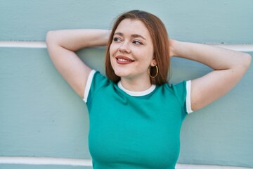 Young redhead woman smiling confident standing with hands on head over isolated green wall