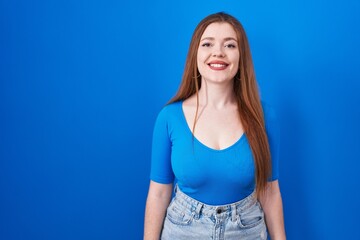 Redhead woman standing over blue background with a happy and cool smile on face. lucky person.