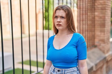 Young redhead woman looking to the side with serious expression at street