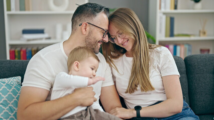 Family of mother, father and baby smiling sitting on the sofa at home