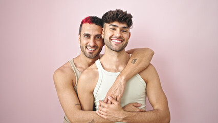 Two men couple smiling confident hugging each other over isolated pink background