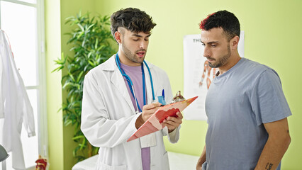 Two men doctor and patient writing medical report at clinic